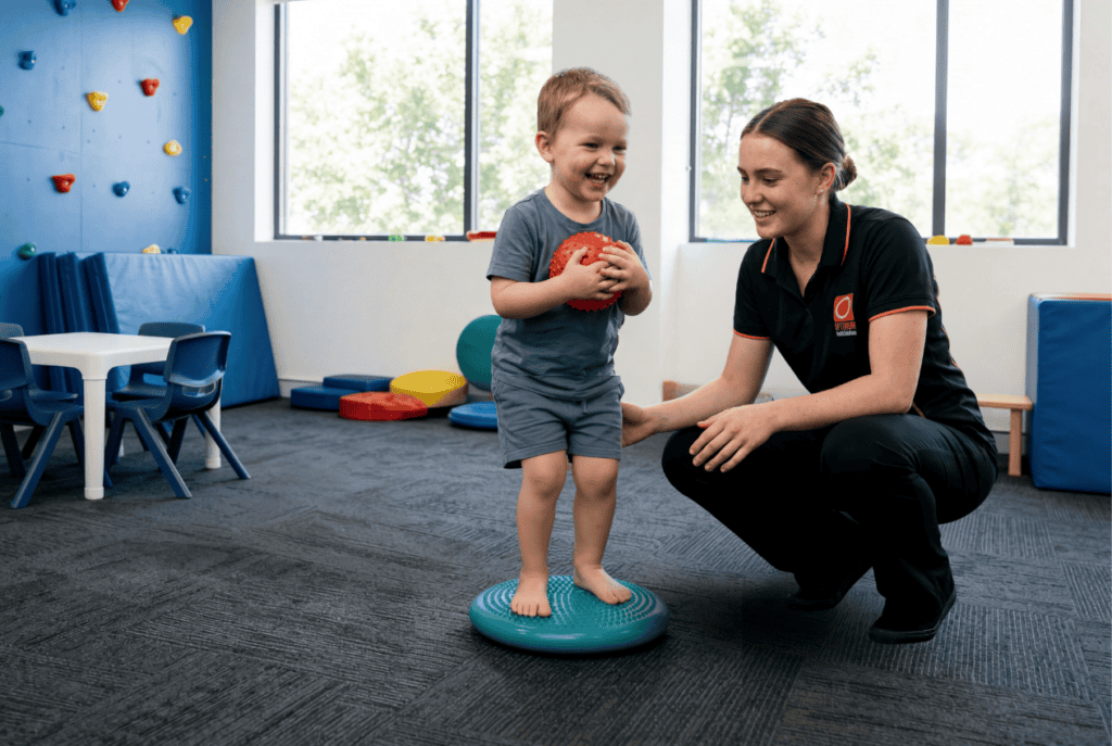 a paediatric physiotherapist encourages a child in their training against toe walking