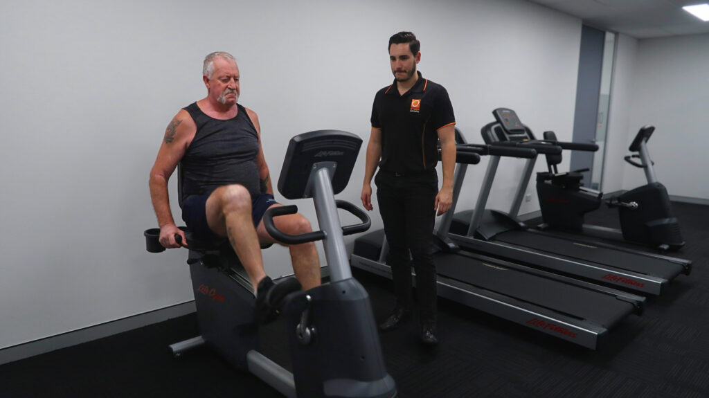 An older man on an exercise bike being instructed by an optimum employee